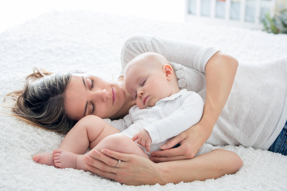 A mother and her baby resting together on a bed in soft back light