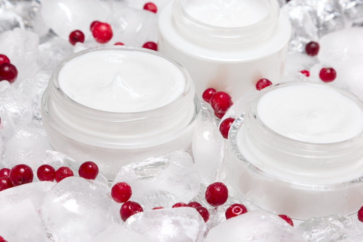 Glass jars of face cream standing among ice cubes and red berries