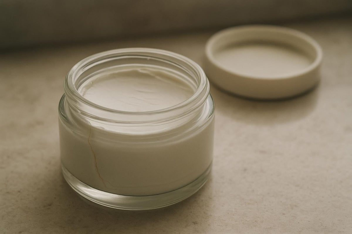 Close-up of an open jar of aging face cream whose surface has begun to let go, a thin ring of clear oil pooling at one edge