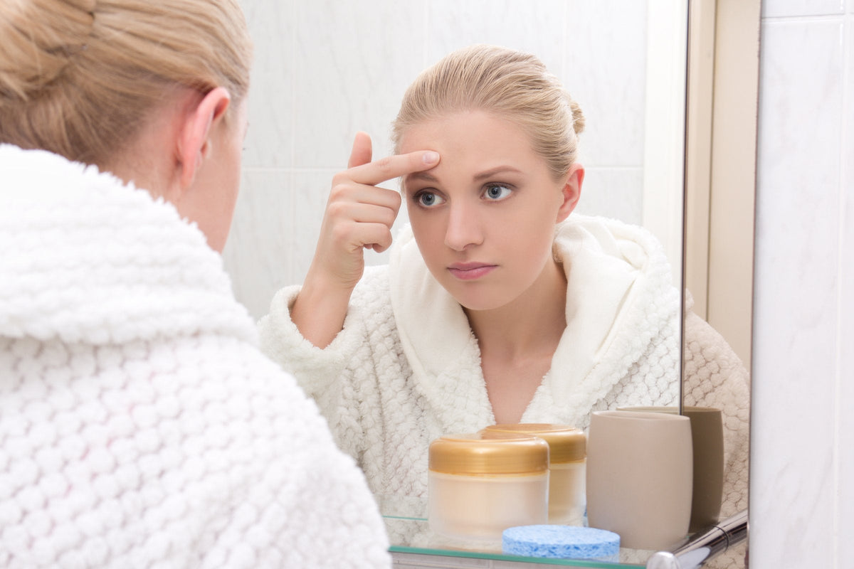 A young woman looking closely at her skin in a bathroom mirror