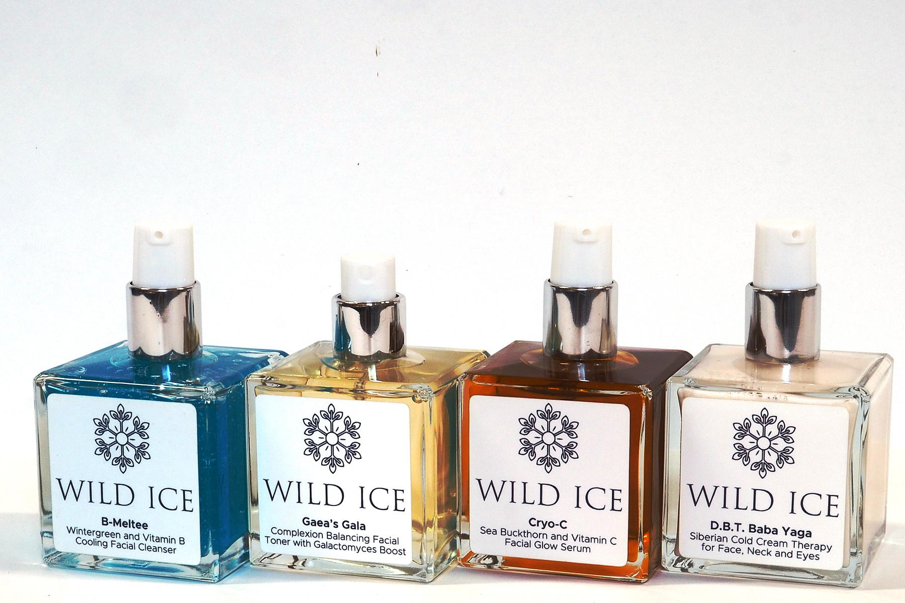 The four full-size Wild Ice Essentials Routine products in a row, B-Meltee cleanser, Gaea's Gala toner, Cryo-C serum and D.B.T. Baba Yaga cream, on a plain pale studio surface