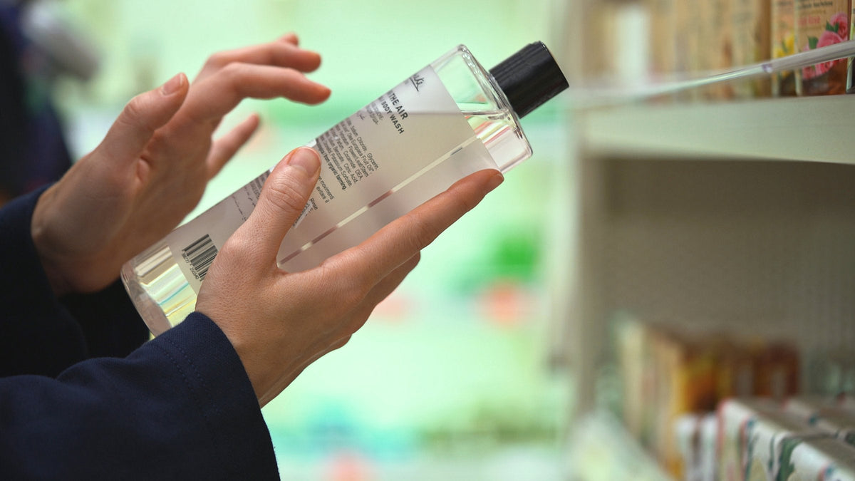 A woman's hands turning a clear bottle to read the ingredient list on its label in a shop