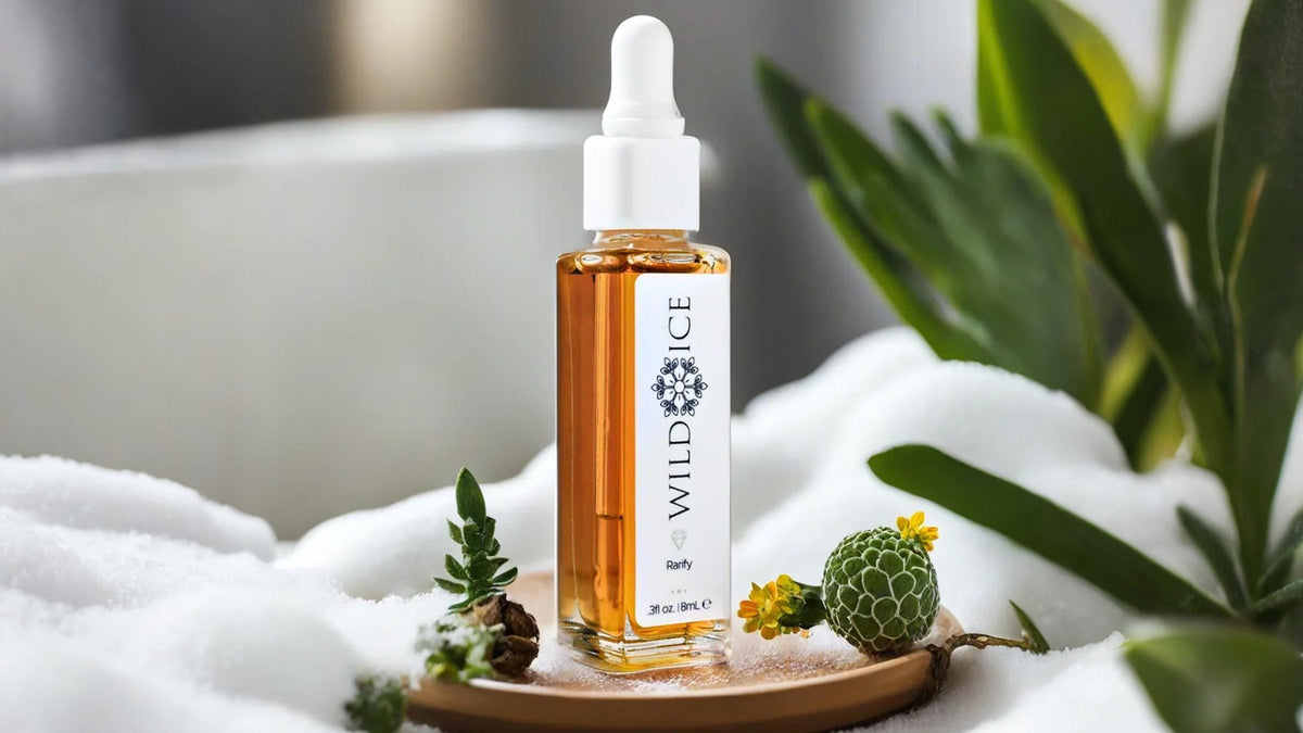A dropper bottle of Rarify, the cold-preserved botanical concentrate for blemish-prone skin, standing on a wooden coaster in snow beside a green seed pod and small flowers